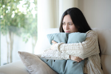 Sad asian woman complaining hugging pillow at home