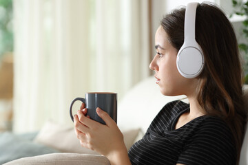 Serious pensive woman listening audio with headphone drinking coffee