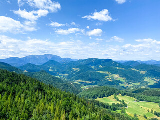 Obraz premium A stunning panoramic view of verdant hills, expansive valleys, and majestic mountains under a bright blue sky with soft, scattered clouds. This serene landscape captures the untouched beauty of nature