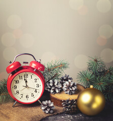 Red retro alarm clock with fir branches and a Christmas tree toy. The clock shows a few minutes until New Year.