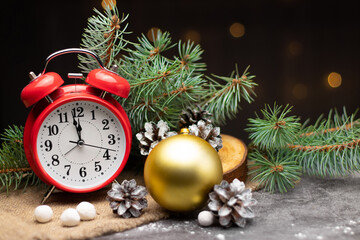 Red retro alarm clock with fir branches and a Christmas tree toy. The clock shows a few minutes...