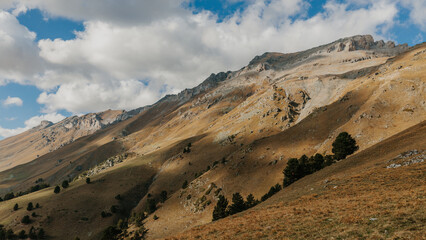 A panoramic view of a mountain range with clouds in the sky and a grassy meadow in the foreground