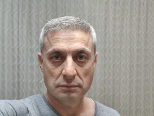 Middle-aged man with a contemplative gaze, embodying wisdom and resilience; a reflection of life's journey etched in his face, set against a neutral patterned background.