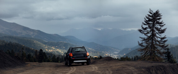 Black SUV driving on a dirt road in the mountains, with a view of a valley and a tall pine tree