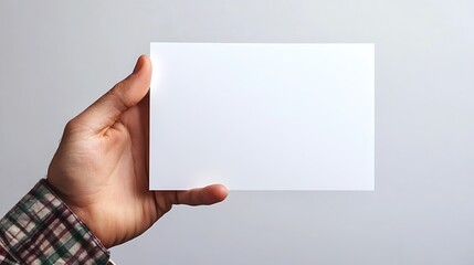 Fototapeta premium A hand holding a blank white card against a neutral background.