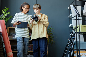 Portrait of two teenage boys working on creative project in studio and looking at pictures on camera screen, copy space