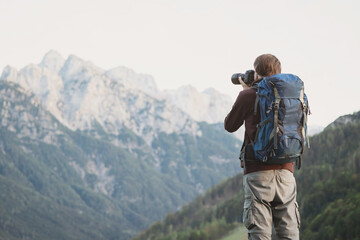 Young cheerful man photographer taking photographs with digital camera in mountains. Travel and active lifestyle concept