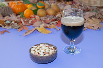 Black beer and a bowl of roasted peanuts accompanied by autumn leaves and fruits on the table.