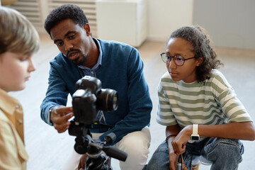 Portrait of African American man as male teacher helping children setting up video camera for...