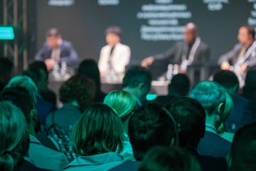 Crowd of professionals attending business conference, focusing on speakers in panel discussion....