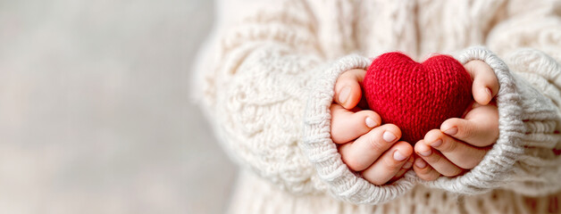Child Holding Knitted Red Heart in Hands as a Symbol of Love, Care, and Warmth. Giving Tuesday ,Day of Charity, Valentines day concept