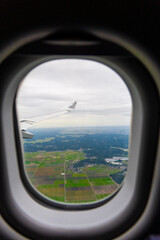 View of green farmland and cityscape from an airplane window during a cloudy day