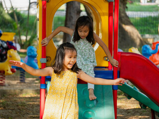 Cute sisters having fun on a colorful slide in an outdoor park. Children playing in the playground during summer vacation.