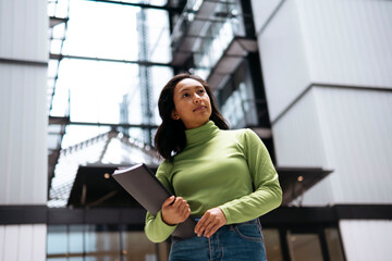 Thoughtful businesswoman standing with file folder outside office building