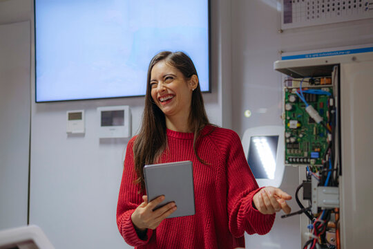 Happy engineer standing with tablet PC near machine in office