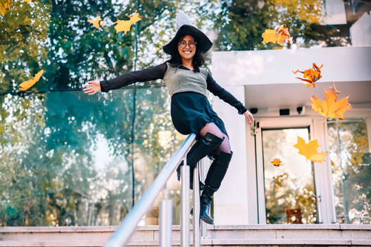 Smiling woman in witch costume sitting on railing