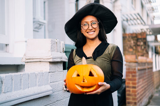 Smiling woman in witch costume holding Halloween pumpkin