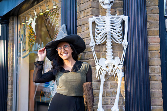 Cheerful woman in witch costume standing by human skeleton