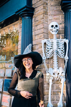 Happy woman in witch costume standing by human skeleton