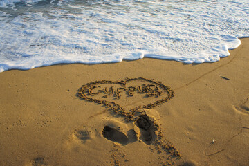 Simple heart drawn in sand on a sunny beach with gentle waves lapping at the shore.