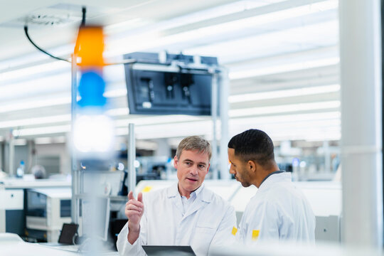 Technicians in lab coats discussing in electronics factory