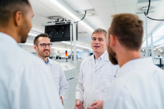 Team of competent electrical technicians in lab coats having meeting in electronics factory