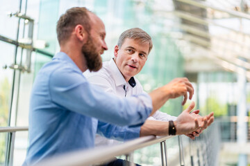 Colleagues discussing innovative business solutions leaning standing in office corridor