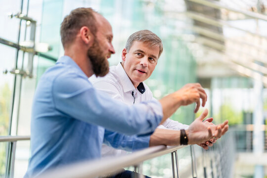 Colleagues discussing innovative business solutions leaning standing in office corridor