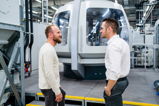 Employee and businessman talking at modern machine in a factory