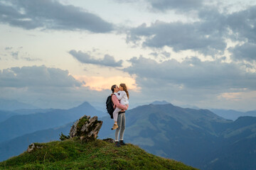 Mother carrying daughter and kissing on mountain under cloudy sky