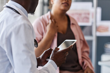 Side view closeup of African American doctor holding tablet while talking to patient during consultation in clinic copy space