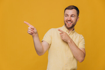 Cute unshaven man in yellow shirt pointing fingers up at copy space isolated on yellow background