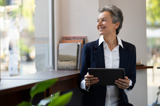 Smiling businesswoman with digital computer standing by window in office