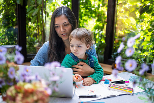 Mother and son using laptop near book at table