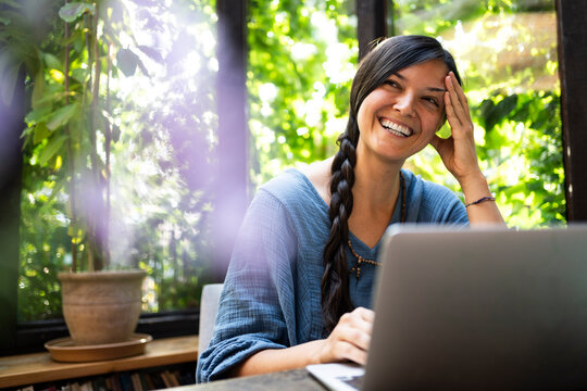 Happy freelancer sitting with laptop at table in gazebo