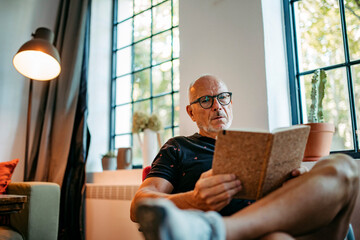 Senior man in community space reading book sitting on bench