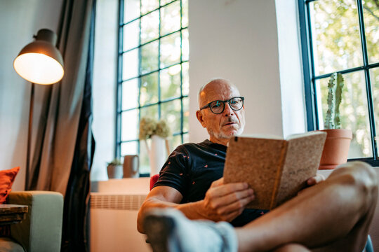 Senior man in community space reading book sitting on bench