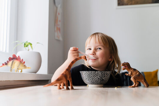 Girl eating breakfast near dinosaur toys at table