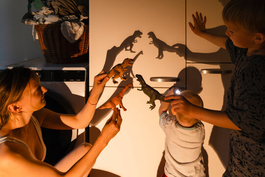 Mother and children creating shadows of toy dinosaurs on closet at home
