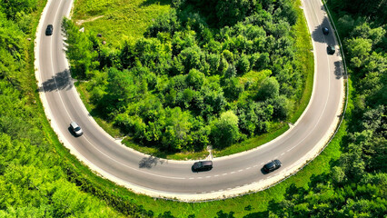 Aerial view of cars on a curved forest road. Aerial shot of vehicles driving along a winding road...