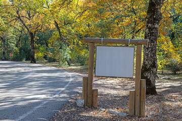 A wooden sign by the roadside in a forest with autumn colors.