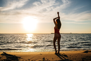 A girl in a red swimsuit on the beach at sunset