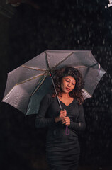 A woman is holding an umbrella in the rain. The umbrella is silver and has a black handle. The woman is wearing a black dress and she is enjoying the rain