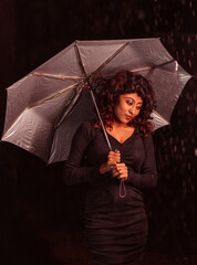 A woman is holding an umbrella in a dark room. Scene is mysterious and somewhat ominous