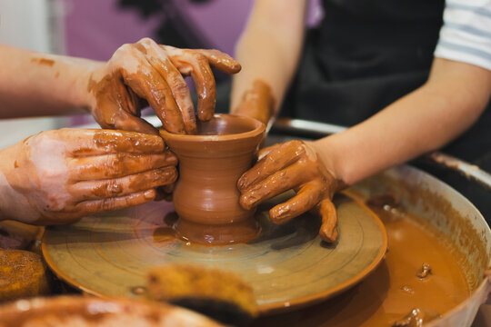 Hands of man teaching boy making bowl on pottery wheel in workshop