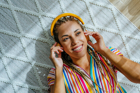Happy woman listening to music through wireless headphones and relaxing on carpet at home