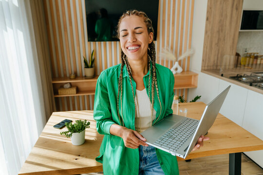 Cheerful freelancer standing with laptop at table
