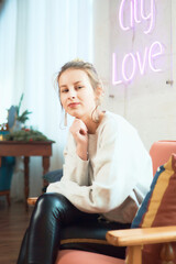 portrait of a teenage girl near a white wall with a pink neon sign, studio photo session