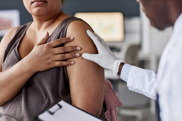 Over shoulder shot of African American doctor examining female patient in clinic and looking at...