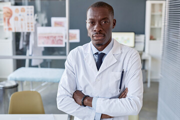 Waist up portrait of adult African American man as doctor in lab coat looking at camera and standing with arms crossed copy space